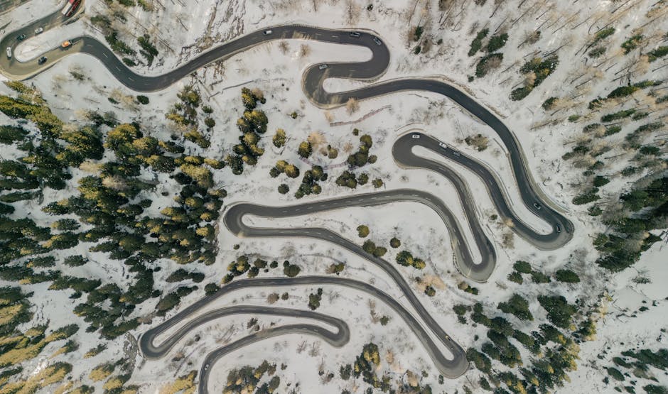 Aerial shot of winding mountain roads surrounded by snowy forest, showcasing winter landscape beauty.